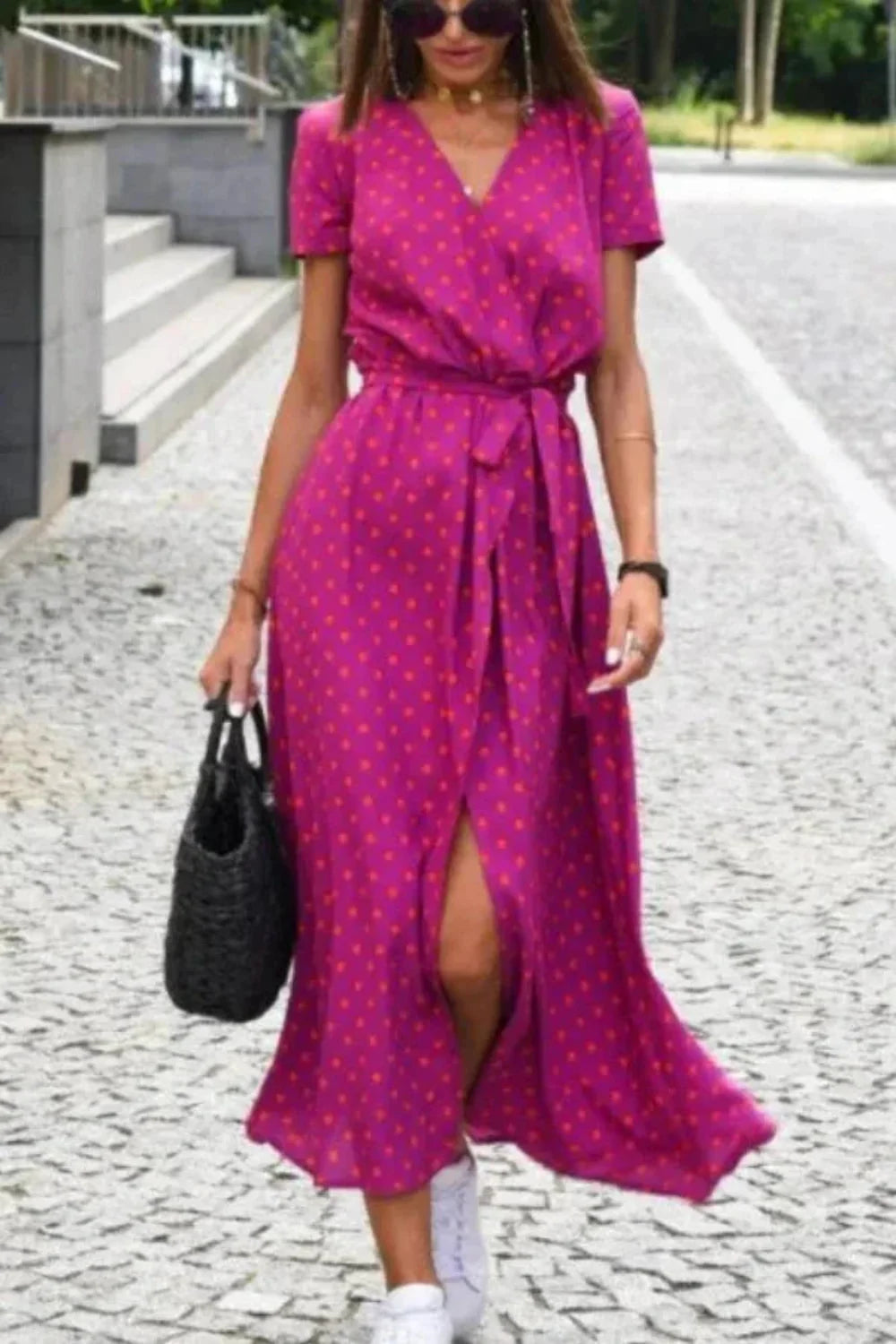 Model wearing the Aleia magenta polka dot wrap midi dress, styled with white sneakers and a black bag.