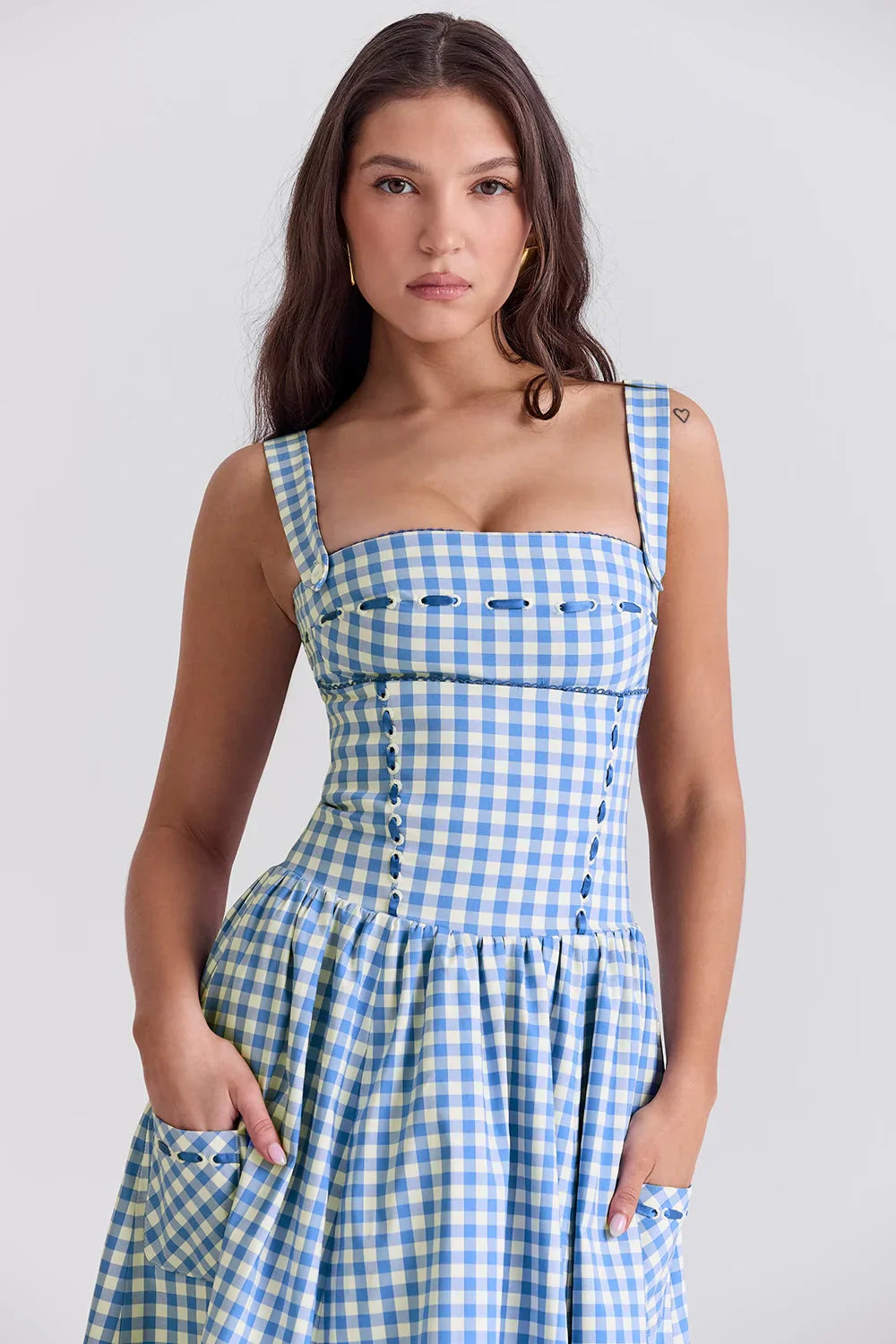 Model wearing the Kouvr Apolline blue gingham midi dress with a structured corset bodice and square neckline, standing in a garden
