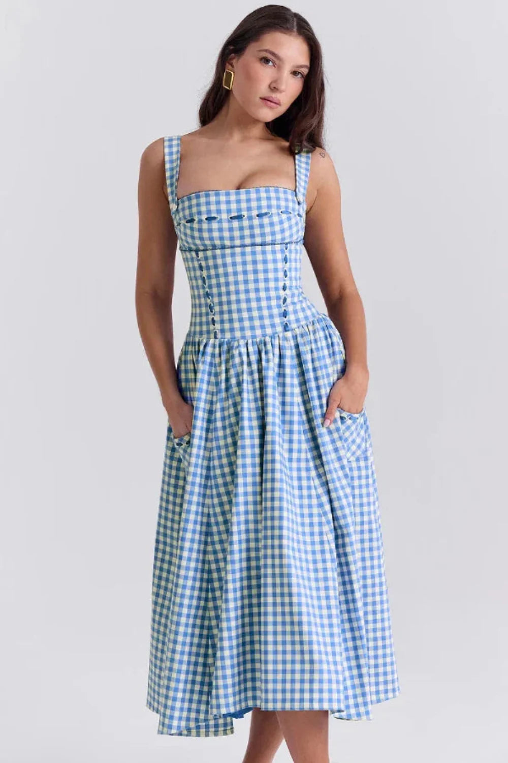 Model wearing the Kouvr Apolline blue gingham midi dress with a structured corset bodice and square neckline, standing in a garden