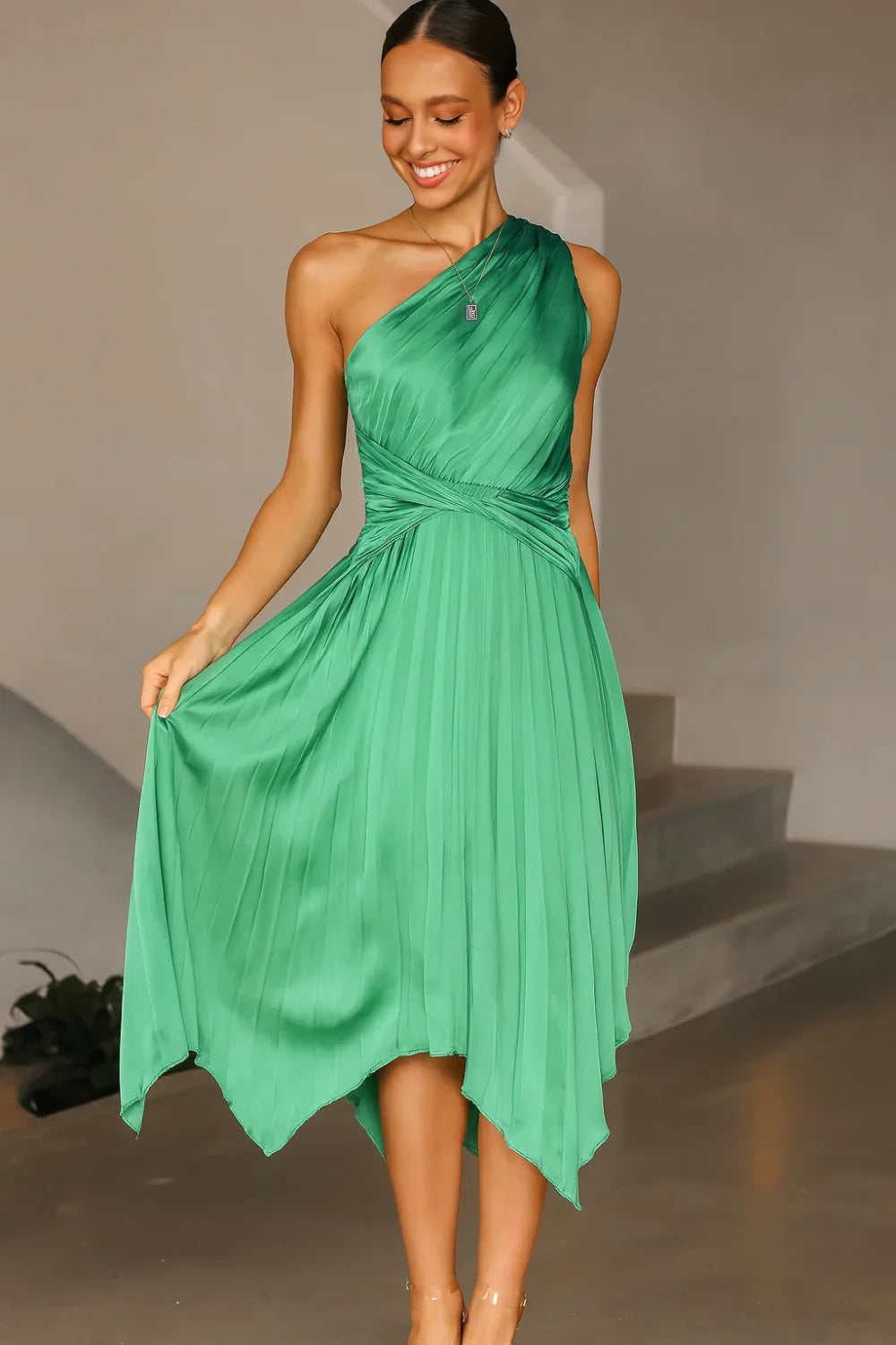 Model poses in the Kouvr Audrine green satin one-shoulder pleated midi dress for a formal event