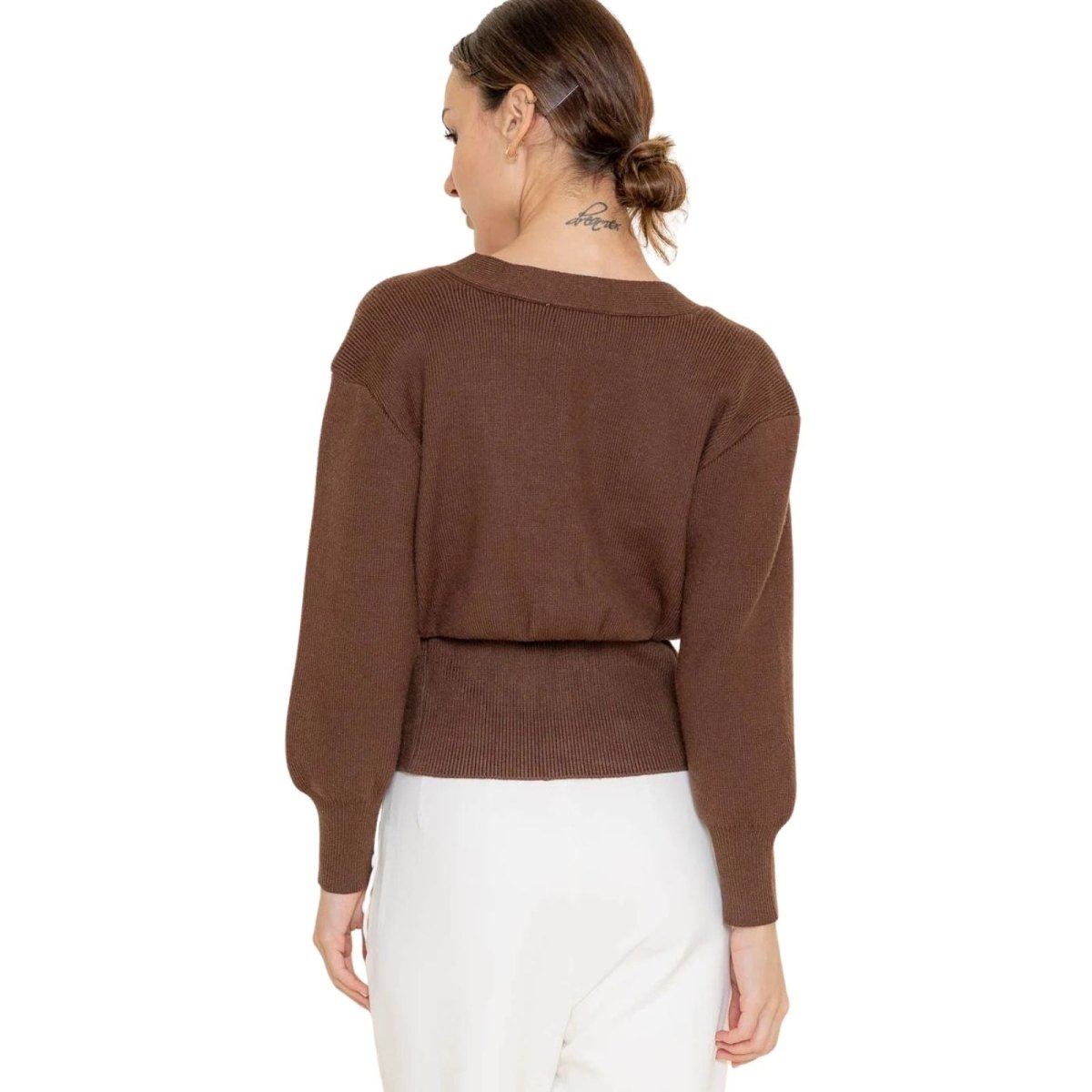 Woman wearing a brown kouvr sweater and white pants on a white background