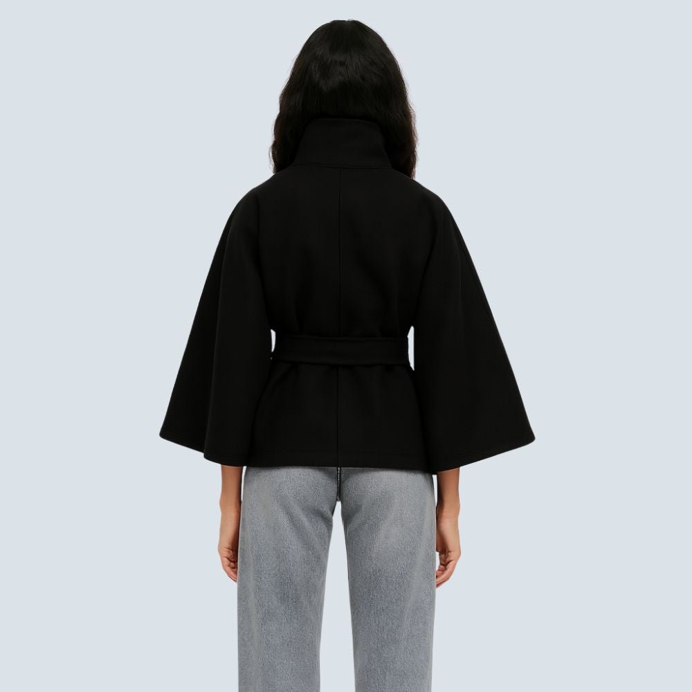 Model wearing the Kouvr black wool funnel neck cape coat with a tie waist belt, styled with light wash denim