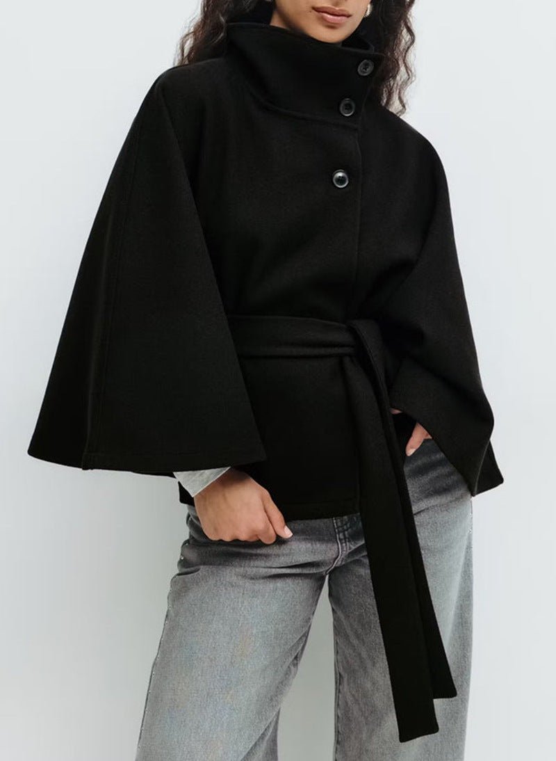 Model wearing the Kouvr black wool funnel neck cape coat with a tie waist belt, styled with light wash denim