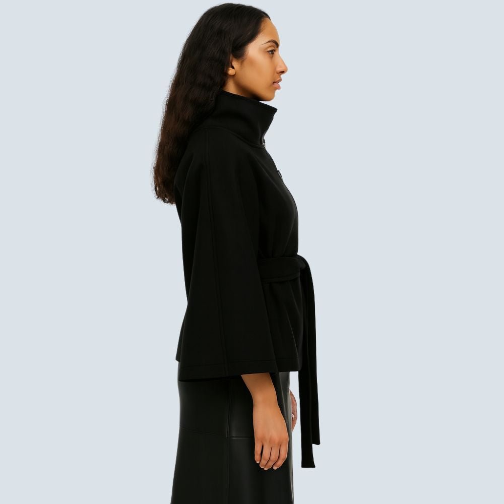 Model wearing the Kouvr black wool funnel neck cape coat with a tie waist belt, styled with light wash denim