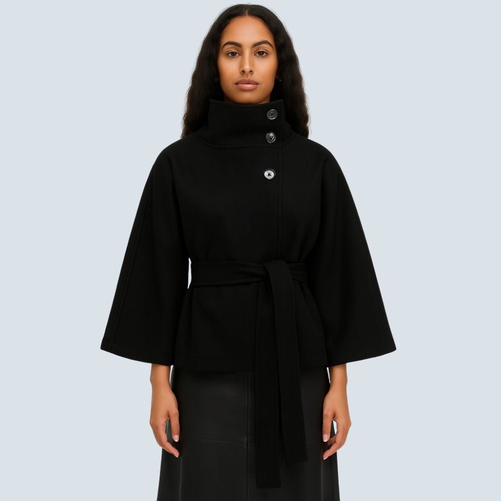 Model wearing the Kouvr black wool funnel neck cape coat with a tie waist belt, styled with light wash denim