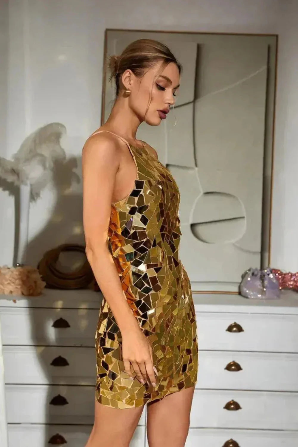 Model wearing Kouvr Brenda gold mirror mosaic halter neck mini dress in a luxury setting