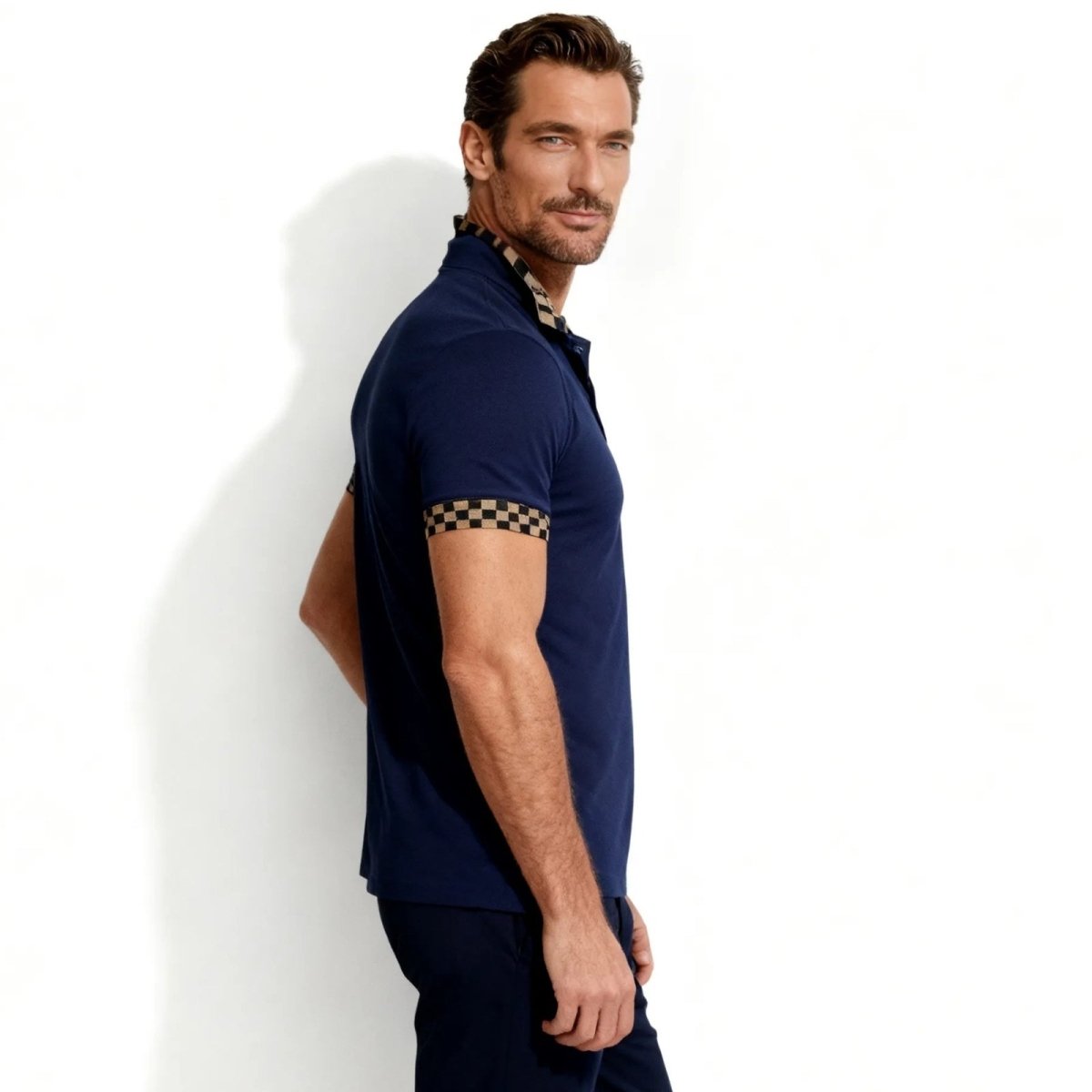 Side profile of a man in a slim fit navy blue designer polo shirt by Kouvr, highlighting the athletic cut and checkered sleeve detail.