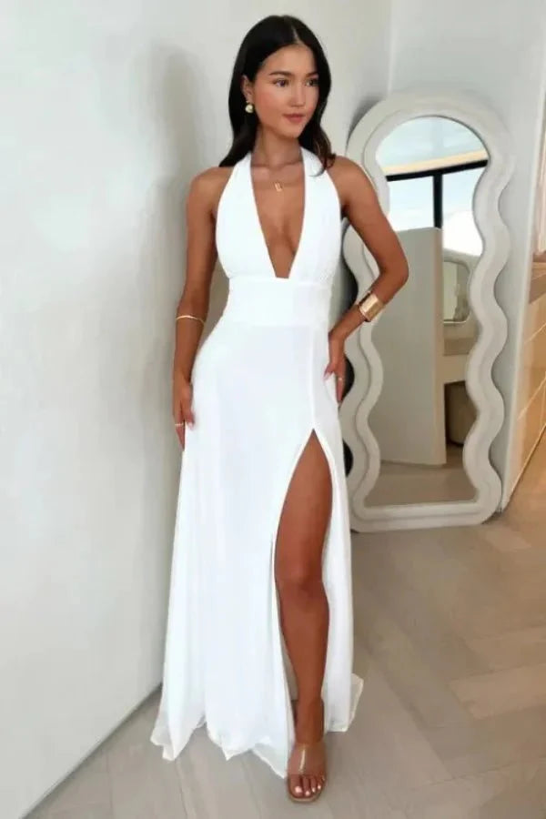 Model wearing the Calanta white halter maxi dress by Kouvr, showing the open back, plunge v-neck, and high leg slit.