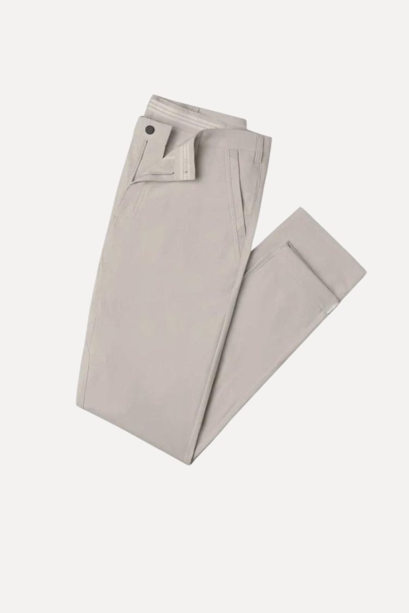 Man wearing Kouvr slim fit tech chinos in stone white with a dark navy t-shirt and white leather sneakers