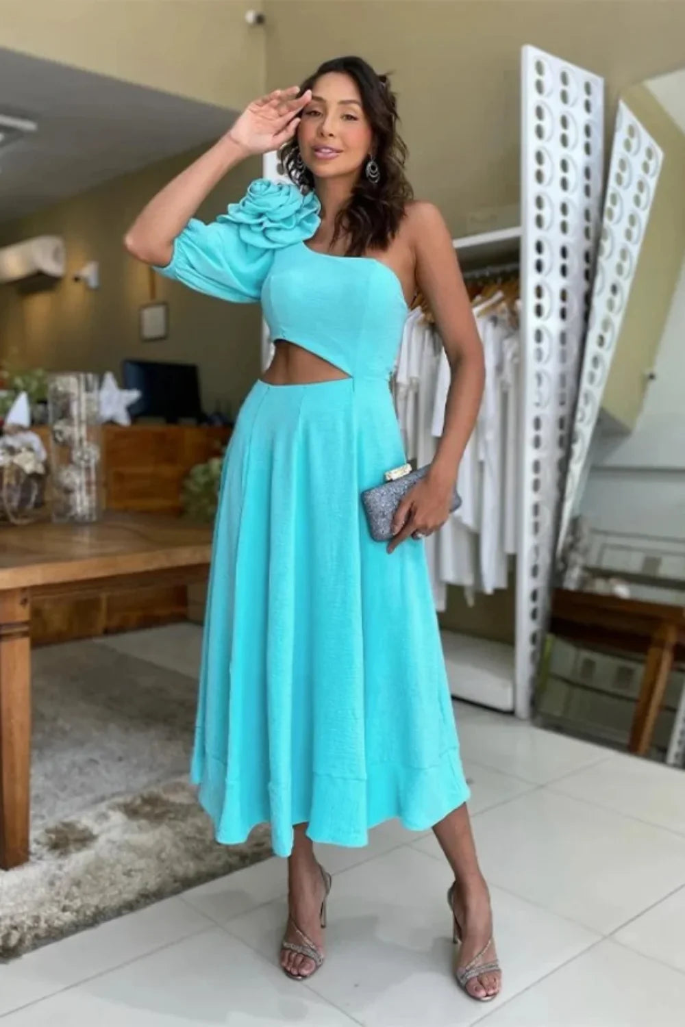 Model standing on a staircase wearing the Kouvr light blue one-shoulder dress with a large flower detail and side cutout