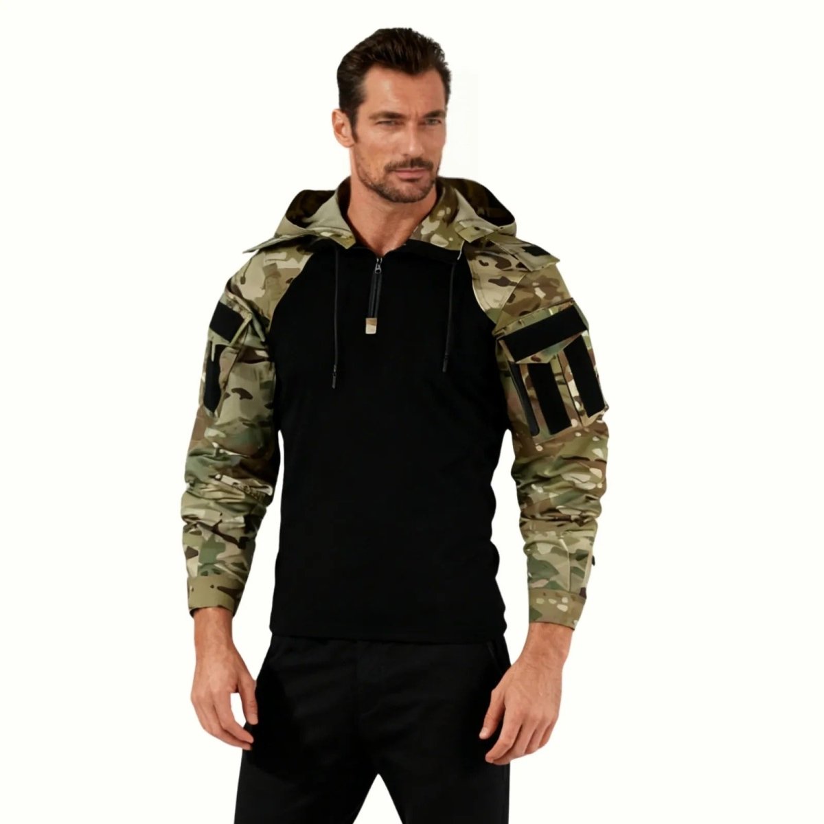 Man wearing the Kouvr Clint tactical combat hoodie featuring a black body and multicam camouflage sleeves and hood, standing against a white background.