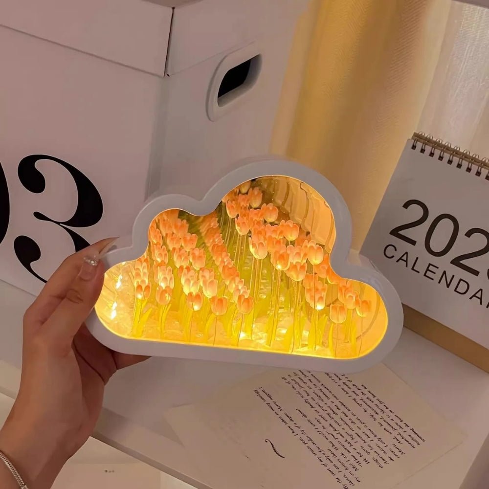 A hand holding the Kouvr Cloud Tulip Infinity Mirror Lamp to show its scale and the intricate detail of the glowing orange tulips inside.