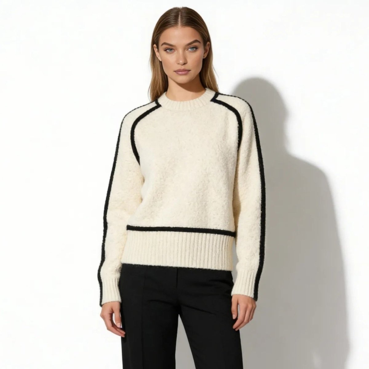 Model wearing Kouvr white wool turtleneck sweater with black contrast trim on sleeves and hem, paired with black trousers.