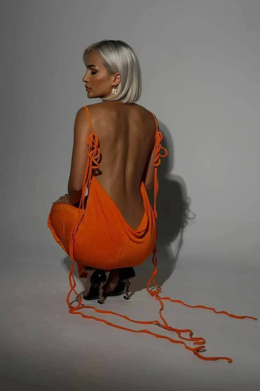 Model wearing Kouvr Fashion's Sunset Orange backless maxi dress with a cowl neck and lace-up back detail