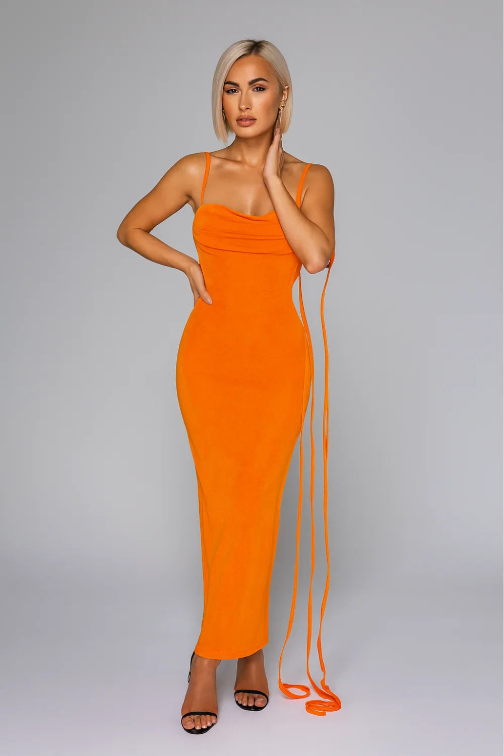 Model wearing Kouvr Fashion's Sunset Orange backless maxi dress with a cowl neck and lace-up back detail