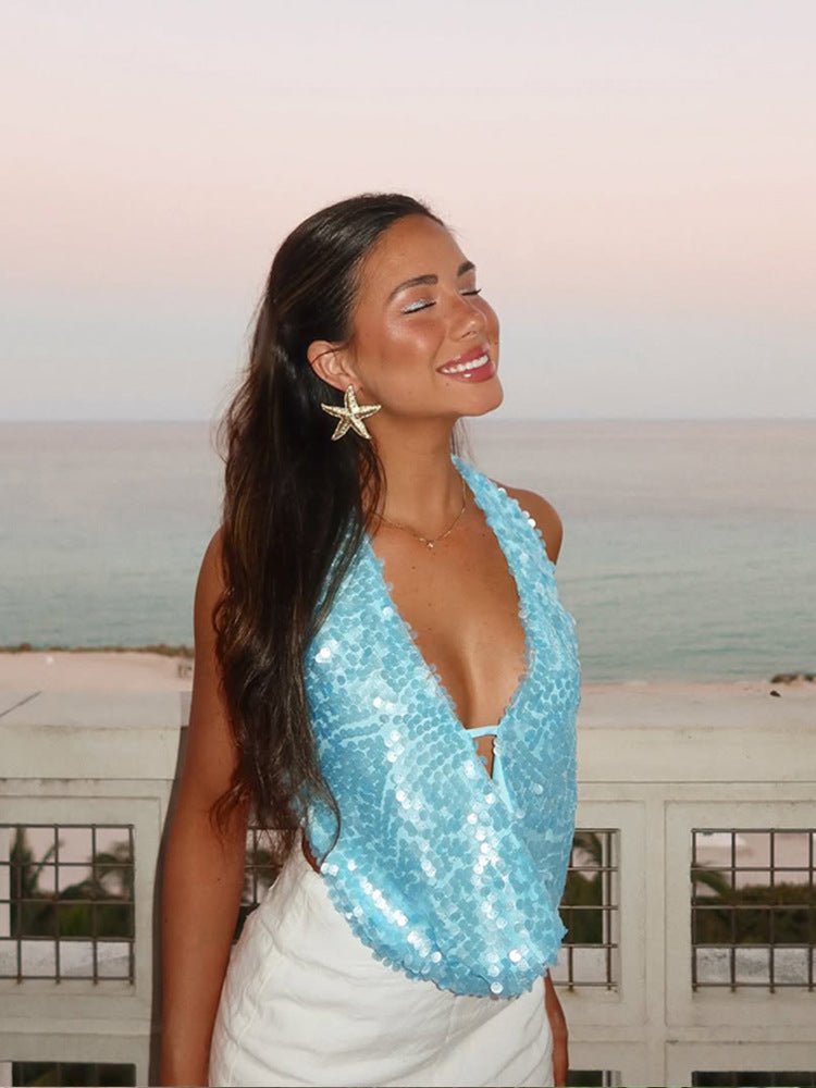 Woman wearing a light blue sequin plunge halter top by Kouvr, looking out over the ocean at sunset, embodying mermaidcore style.
