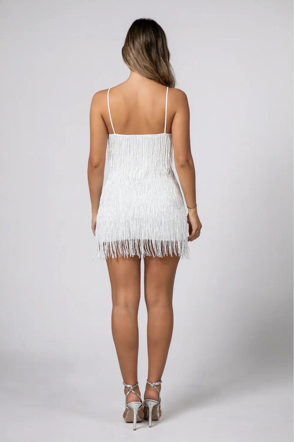 Woman wearing the Kouvr white beaded fringe and feather mini dress at an outdoor event
