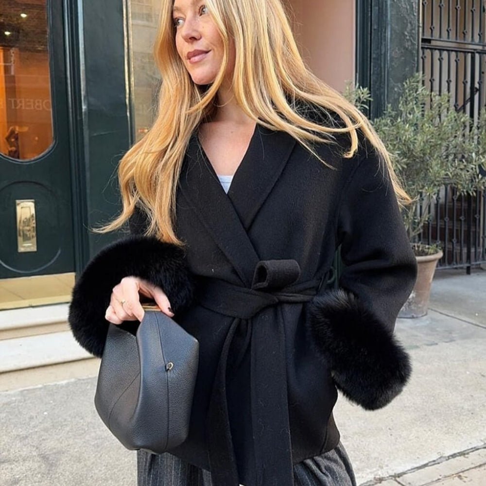 Woman styling the Kouvr Emma black fur cuff jacket on a city street, paired with a black handbag and grey trousers.
