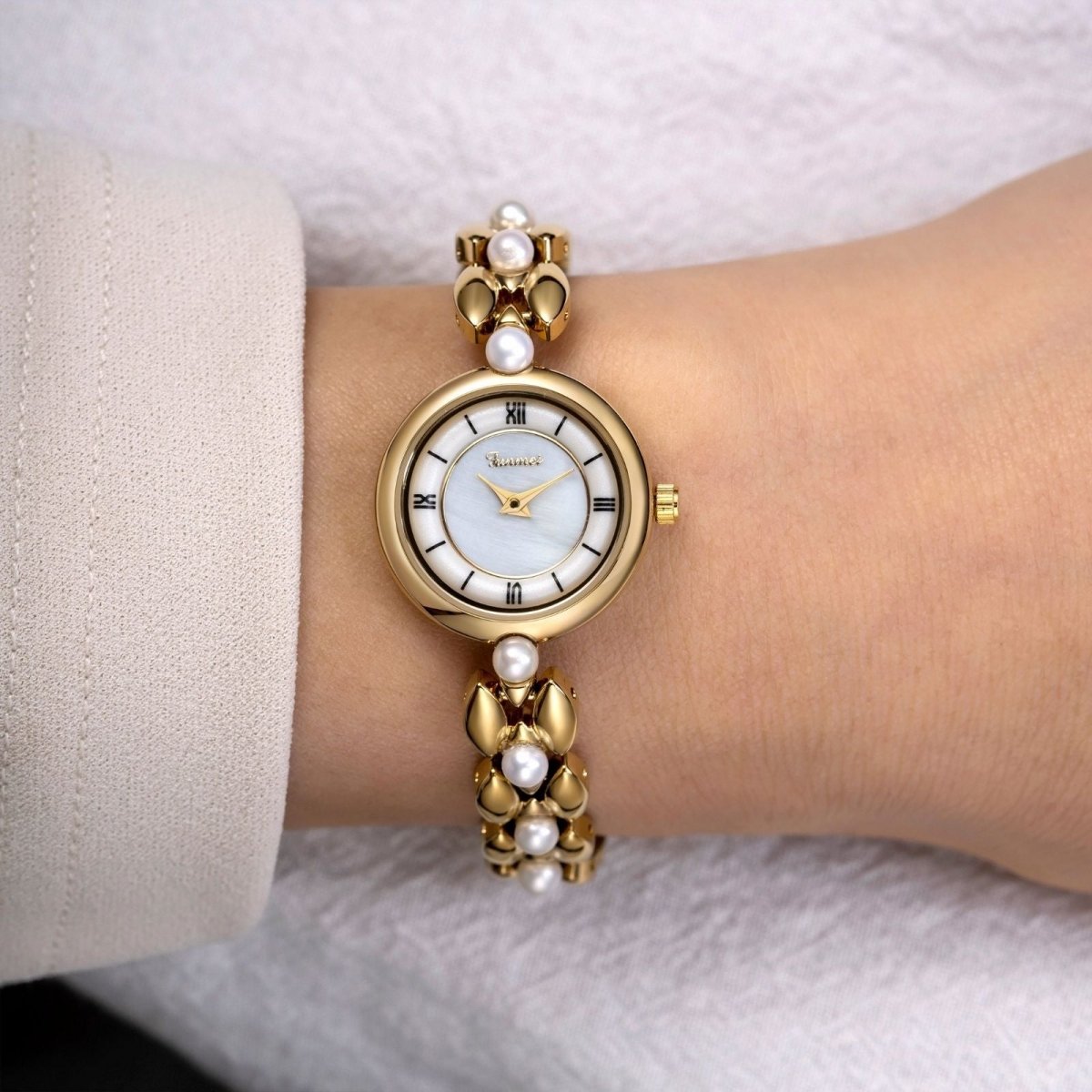 Kouvr Euna Gold and Pearl Bracelet Watch shown on a woman's wrist with a white sleeve.