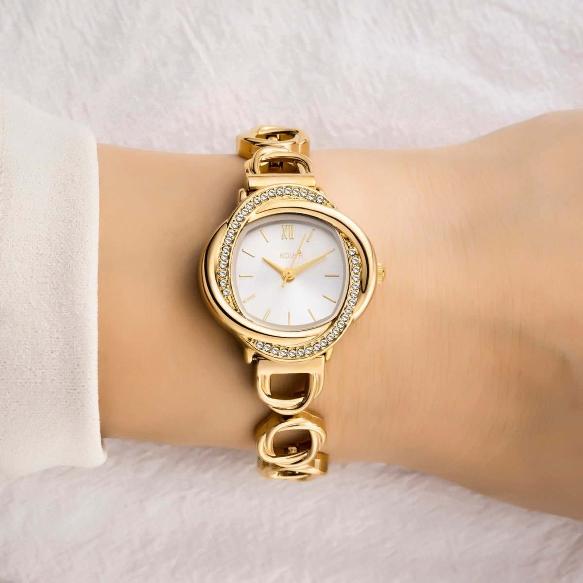 Gold kouvr wristwatch with a white face on a wrist against a white background