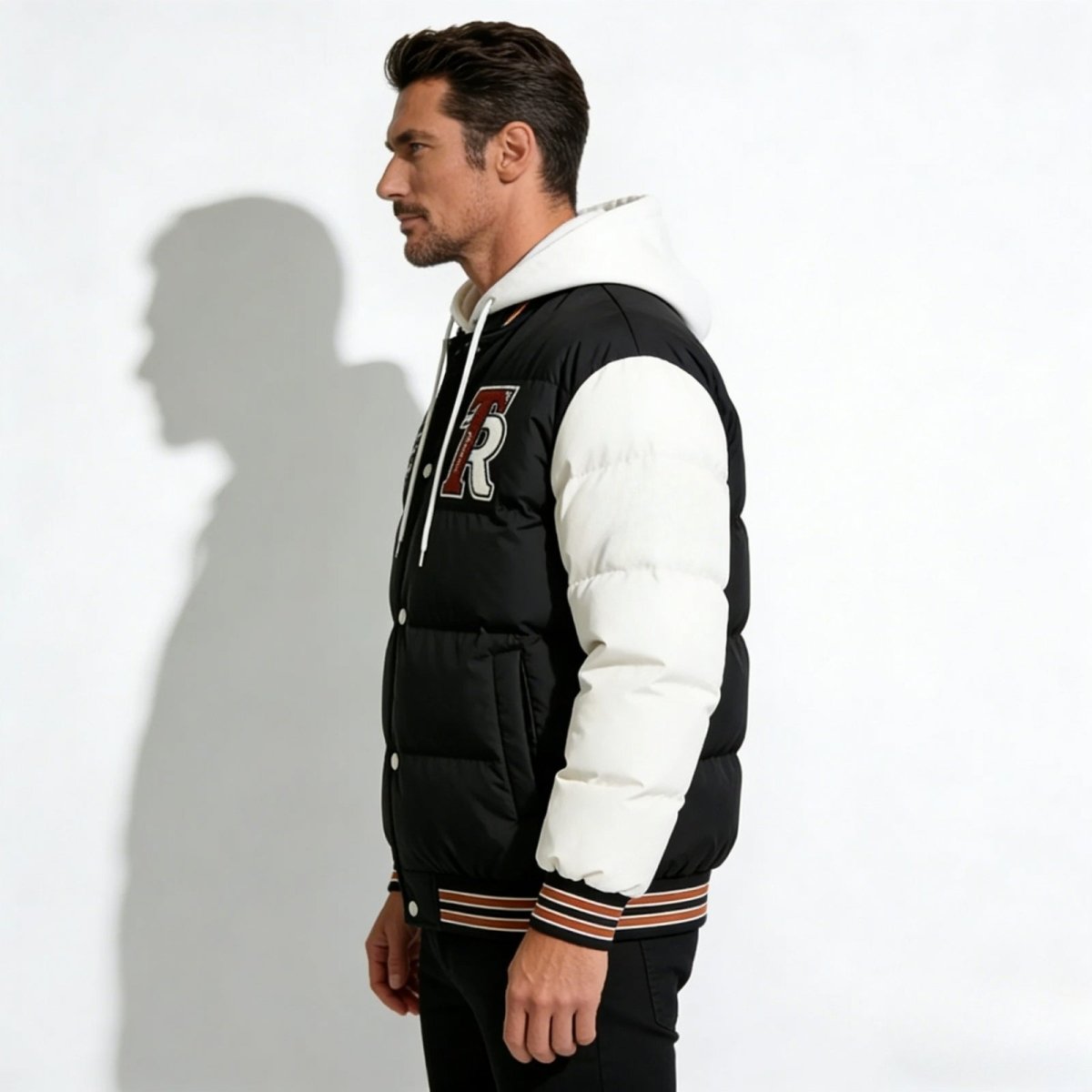Side profile of a man wearing the Kouvr Fashion 'Angelo' black and white varsity puffer, showing the embroidered 'R' and sleeve details.