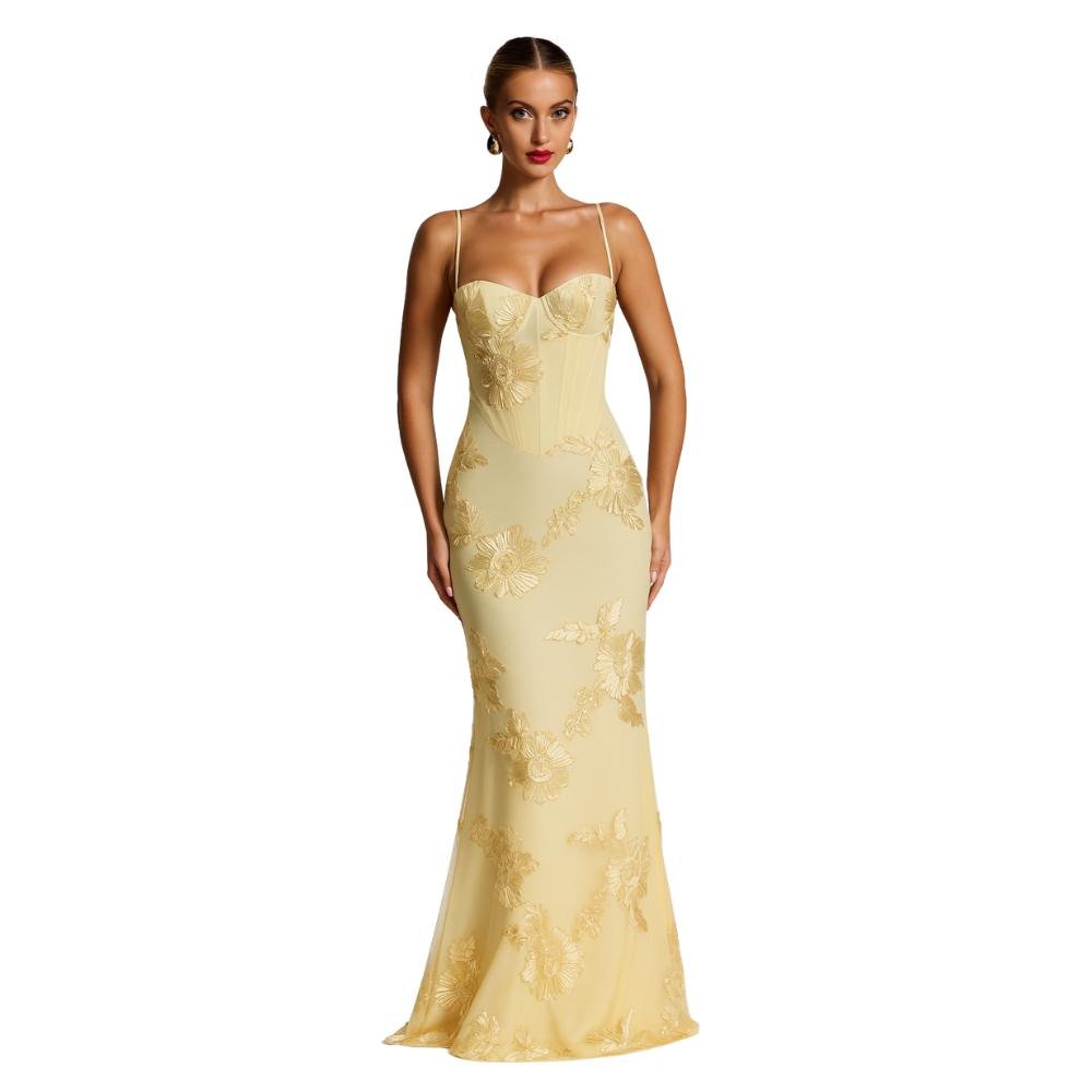 A model viewed from the back wearing the Kouvr Fashion Aphaea Gown, a backless yellow mermaid dress with 3D floral embroidery and an adjustable lace-up corset detail