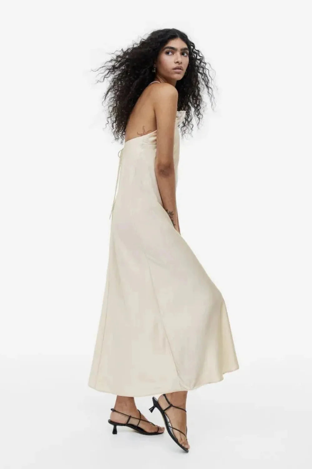 Model from behind wearing the Kouvr Fashion Cathalina beige satin halter dress showing the open back and criss-cross straps