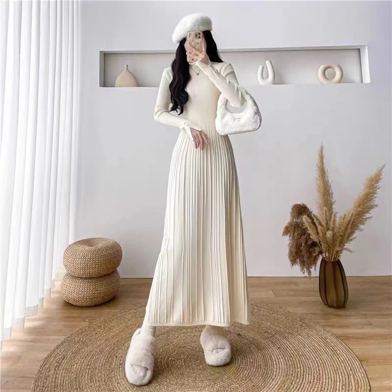 A woman wearing the Kouvr Fashion Dannah long sleeve pleated knit midi dress in ivory, styled with a white beret and fuzzy slippers in a minimalist room.
