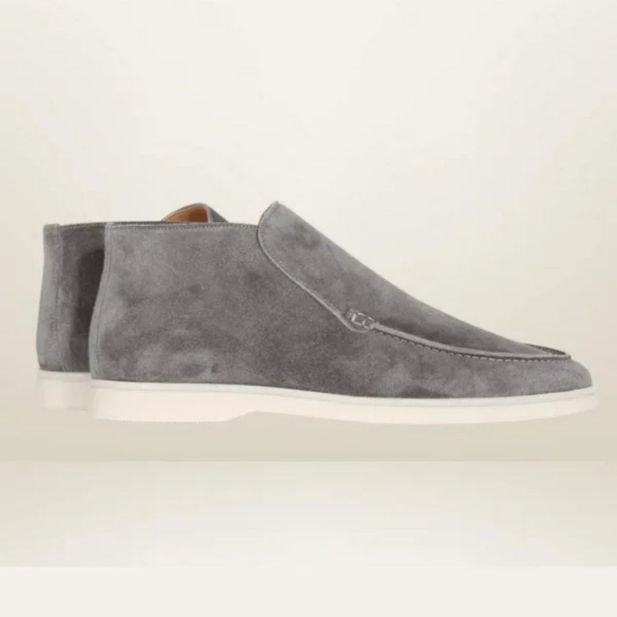 A studio product shot showing the side profile of a pair of men's grey suede loafer chukka boots with a clean white rubber sole.