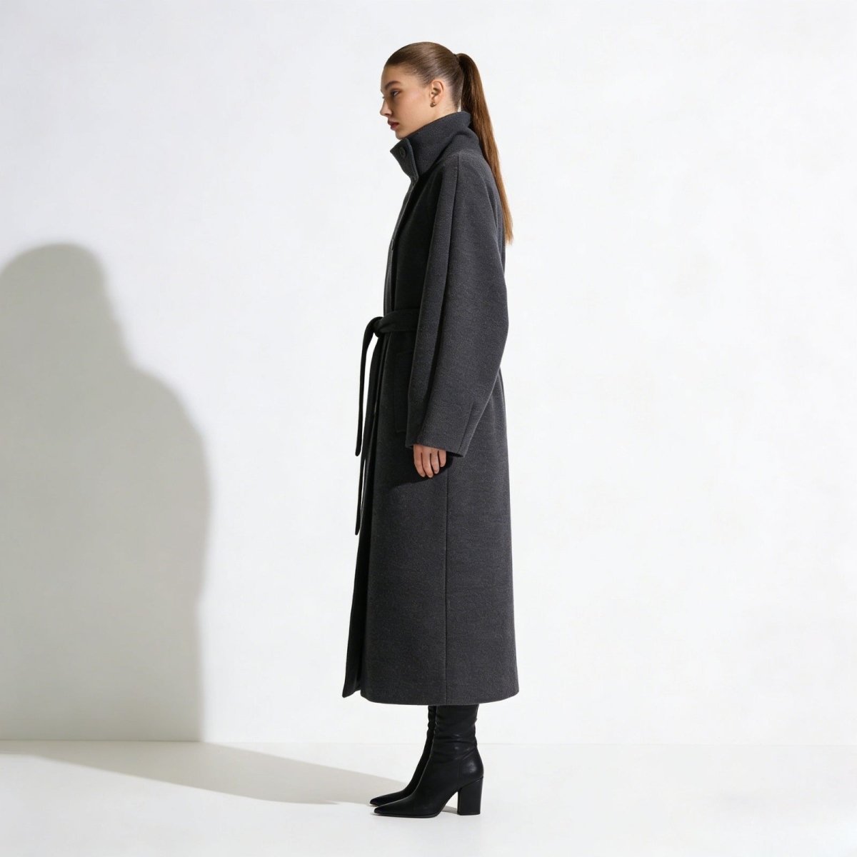 Side profile of a model in the Kouvr Fashion oversized funnel neck wool coat in gray, highlighting the long silhouette and raglan sleeves.