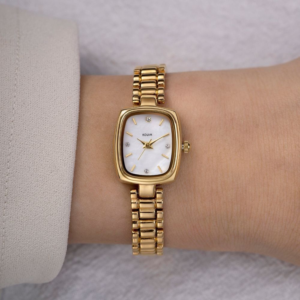 Gold Kouvr wristwatch with a white face on a wrist, against a neutral background