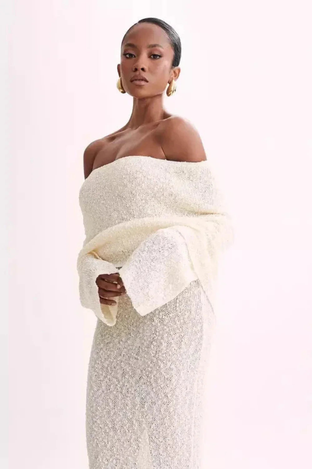 Model wearing Kouvr's ivory off-the-shoulder knit maxi gown, front view
