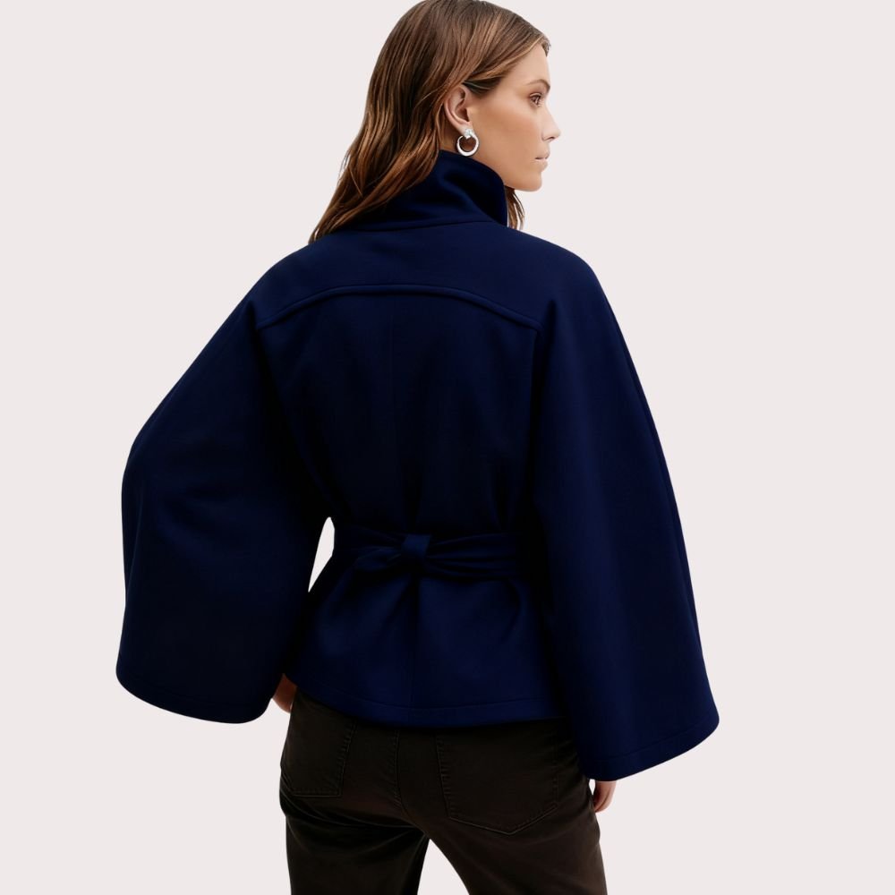 Woman wearing the Kouvr Jaye Cape in navy blue, featuring a high funnel neck, wide sleeves, and a self-tie belt
