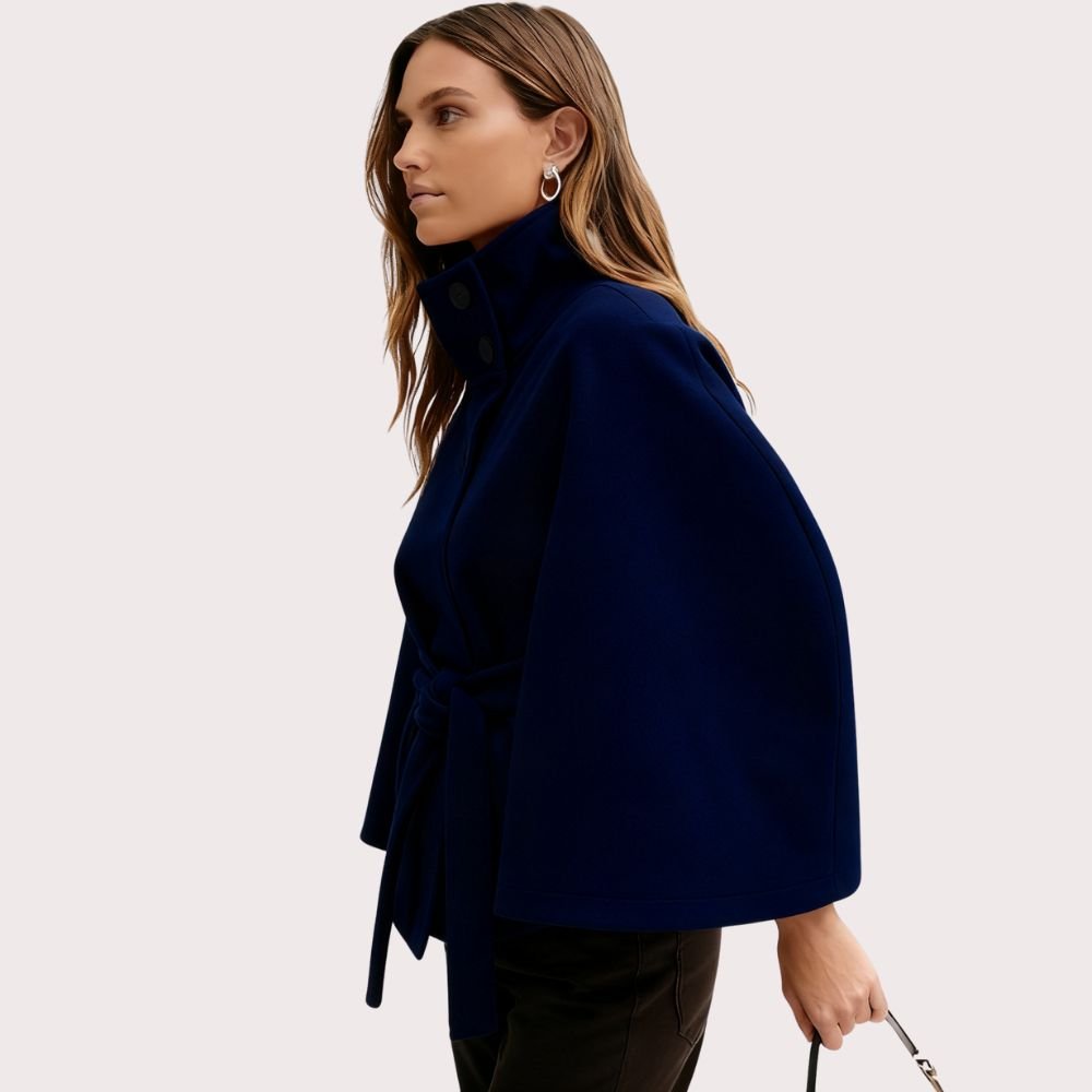 Woman wearing the Kouvr Jaye Cape in navy blue, featuring a high funnel neck, wide sleeves, and a self-tie belt