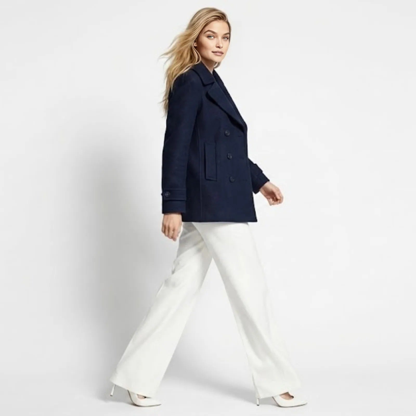 Side view of a model walking in the Kouvr Katherine navy double-breasted peacoat, showcasing its modern boxy silhouette and sleeve shape.