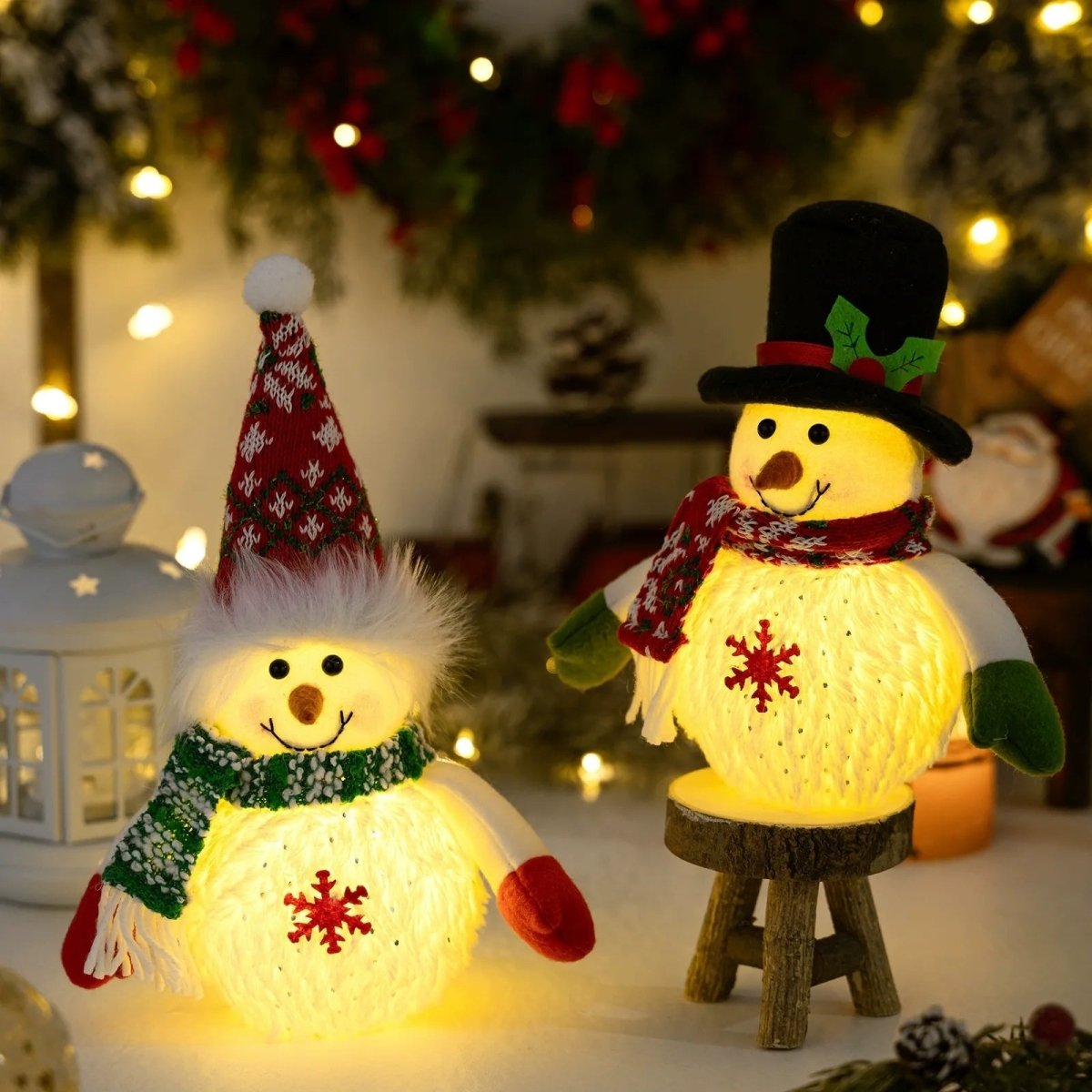 The Kouvr snowman figurine with a top hat sits on a small wooden stool next to its companion, both illuminated in a cozy, festive holiday setting.
