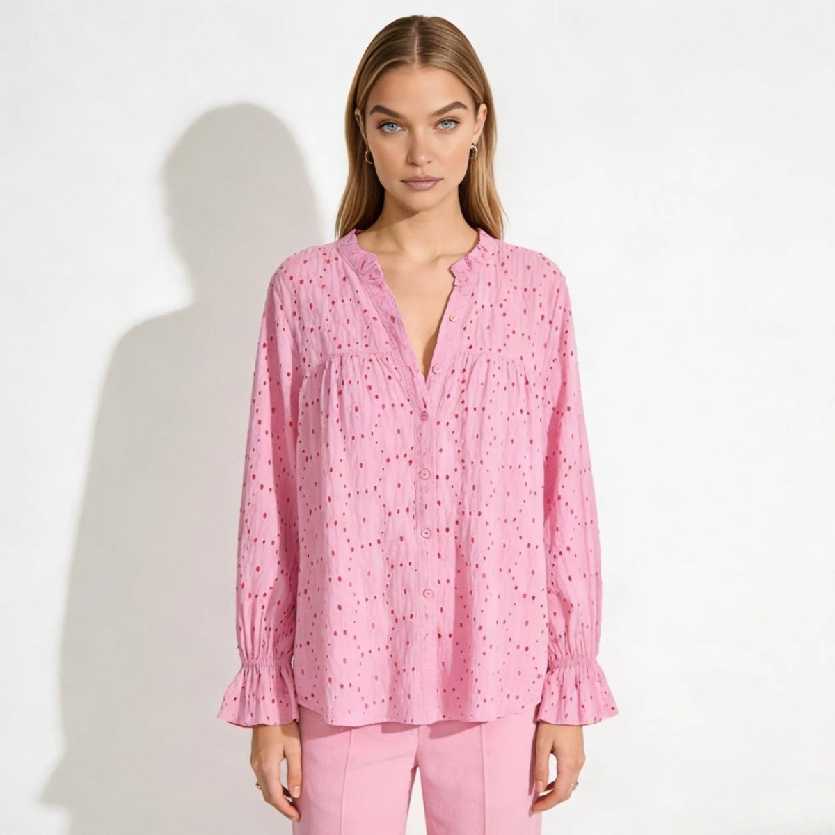Model wearing the Kouvr Lydia long sleeve pink eyelet blouse with matching pink trousers, showing the V-neck and button front.