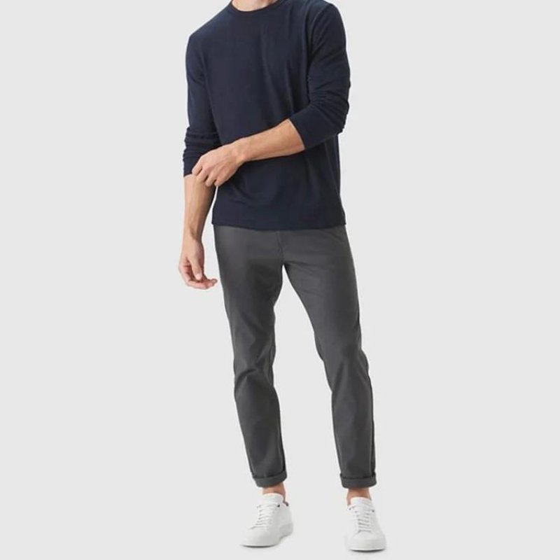 Man wearing Kouvr All-Day Commuter Pants in graphite grey with a dark navy long-sleeve sweater and white sneakers, demonstrating a smart-casual look.