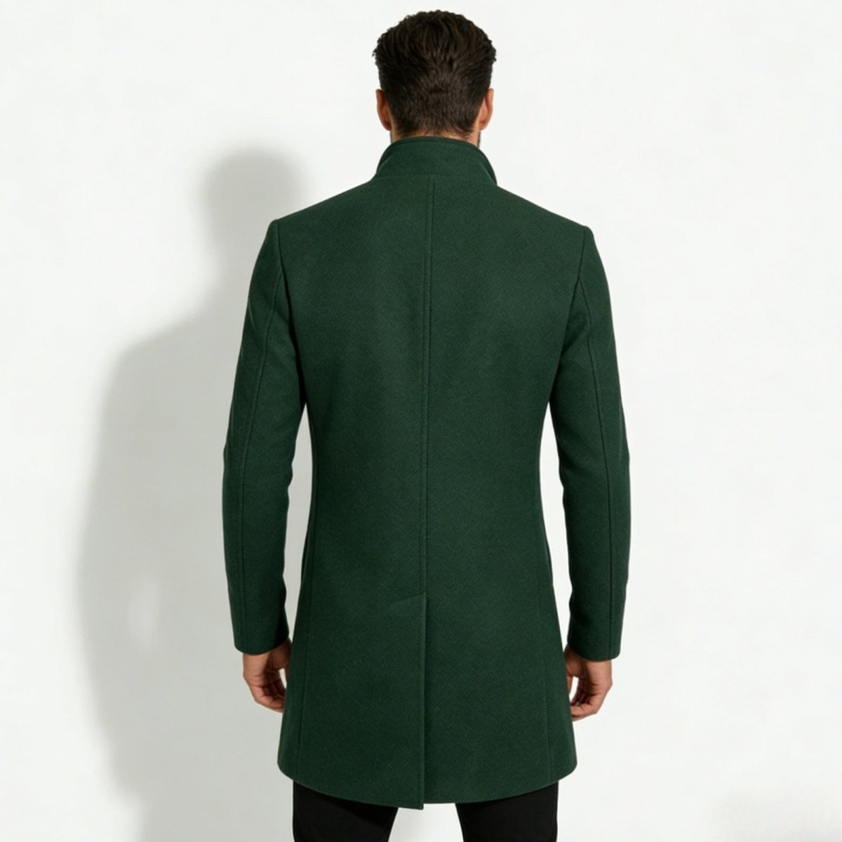 Back view of a man wearing a Kouvr dark green winter overcoat, highlighting the center vent and structured shoulders.