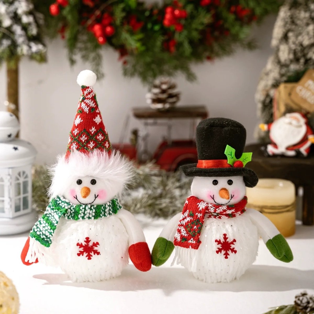 The set of two Kouvr snowman figurines, unlit, displayed on a white surface against a backdrop of Christmas greenery, showing their detailed knit texture.
