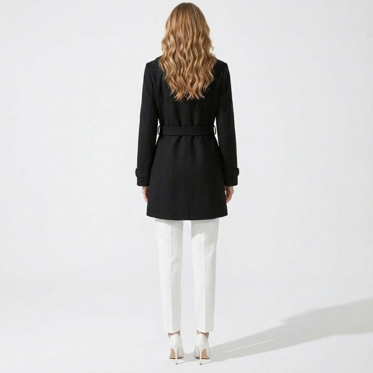 Back view of a model in the Kouvr Priscilla black wool coat, showing the detail of the self-tie belt and the clean lines of the back.