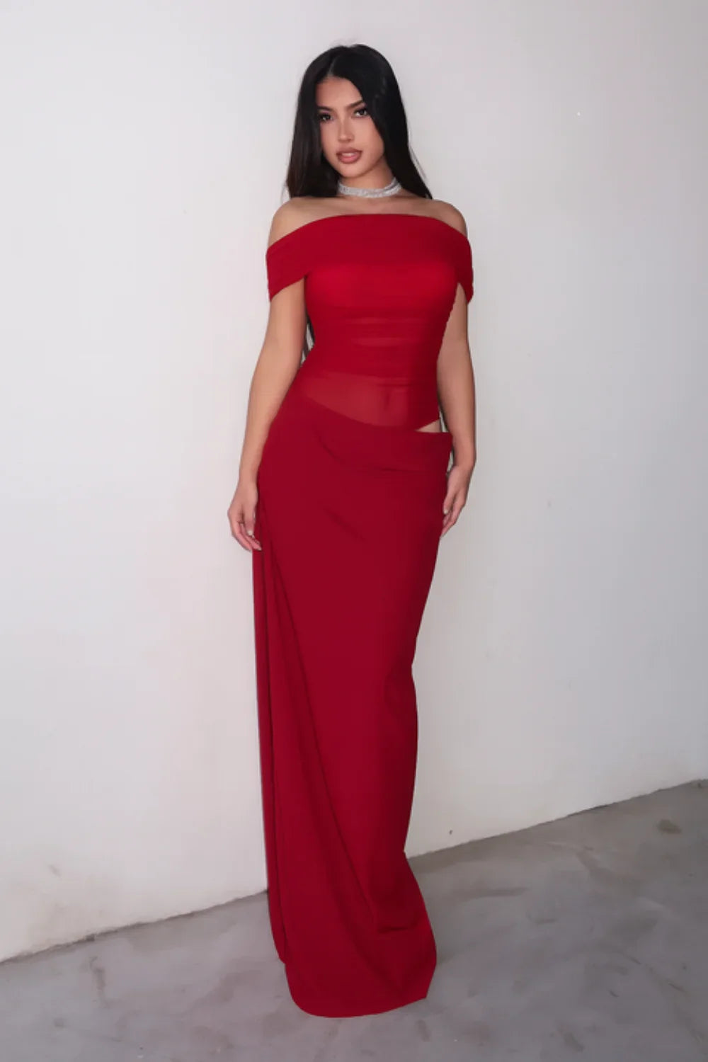 Front view of a woman wearing the Kouvr red off-shoulder formal gown with a sheer waist and hip cutout
