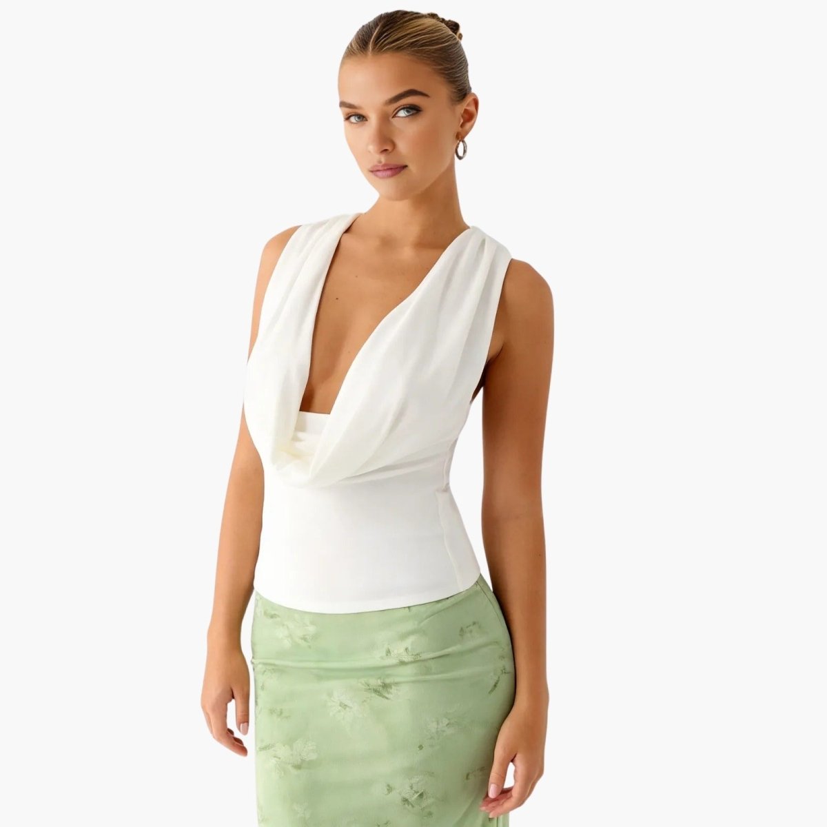 A three-quarter view of a woman wearing a white draped v-neck top with her hair in a bun, showcasing the top's fitted silhouette.