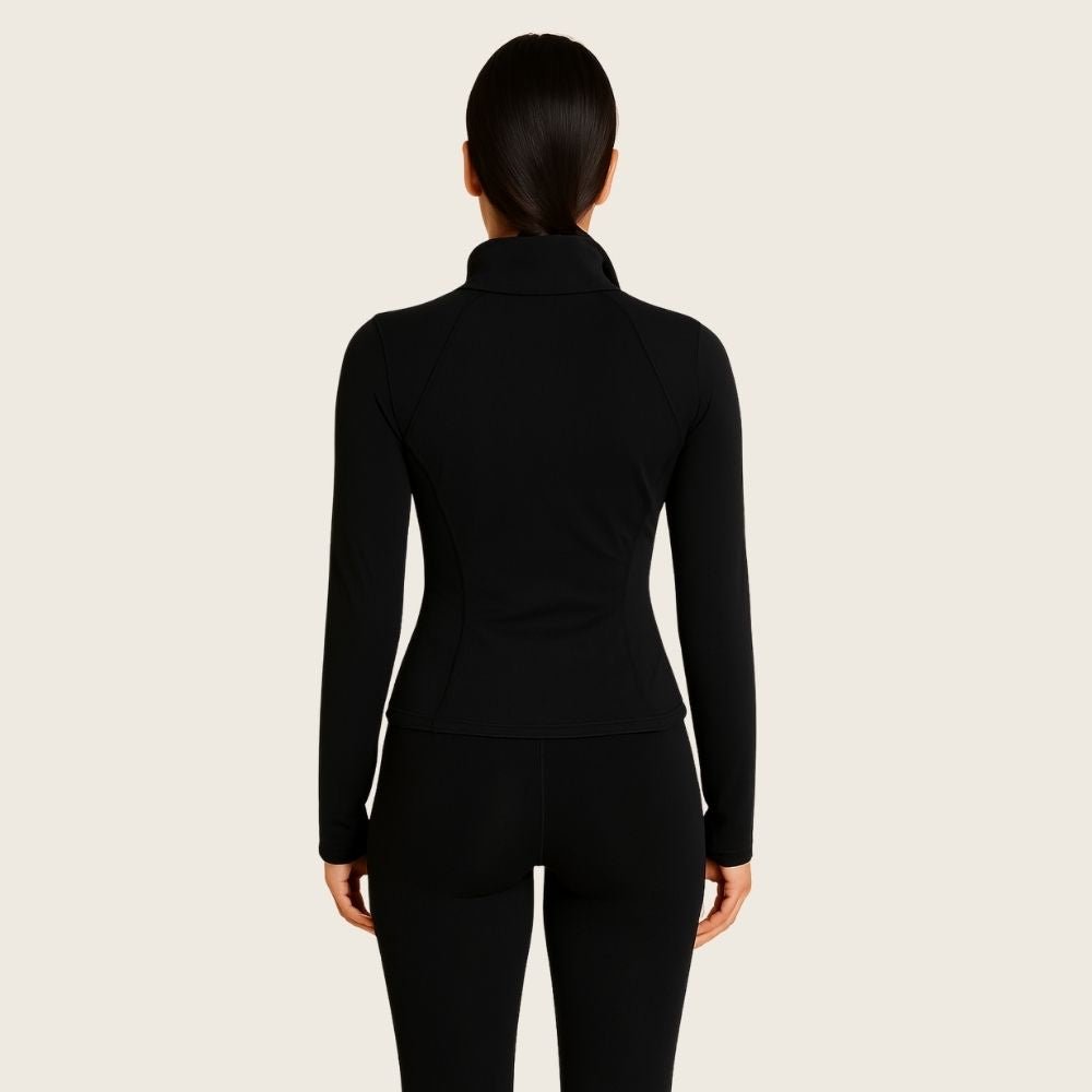 Woman wearing the black Kouvr Sculpting Athletic Jacket in a modern fitness studio.