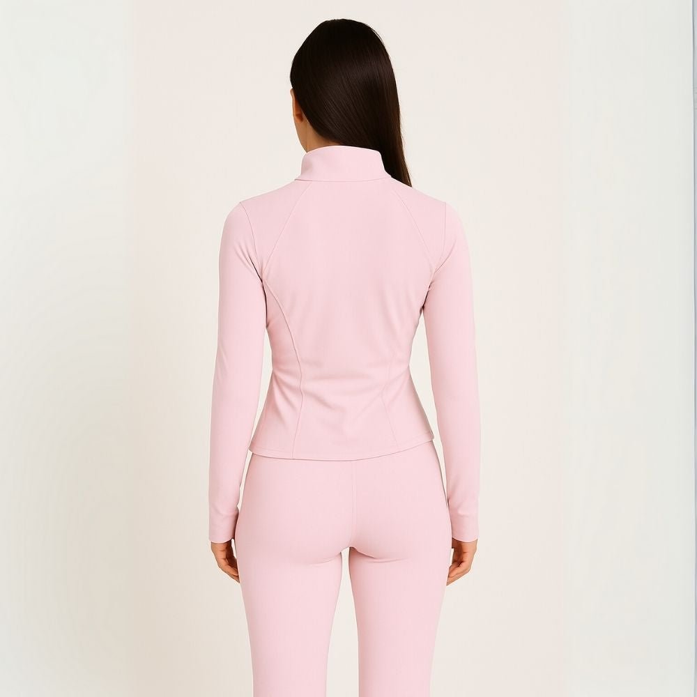 Woman wearing the Kouvr Sculpting Zip Jacket in Petal Pink against a white wall.