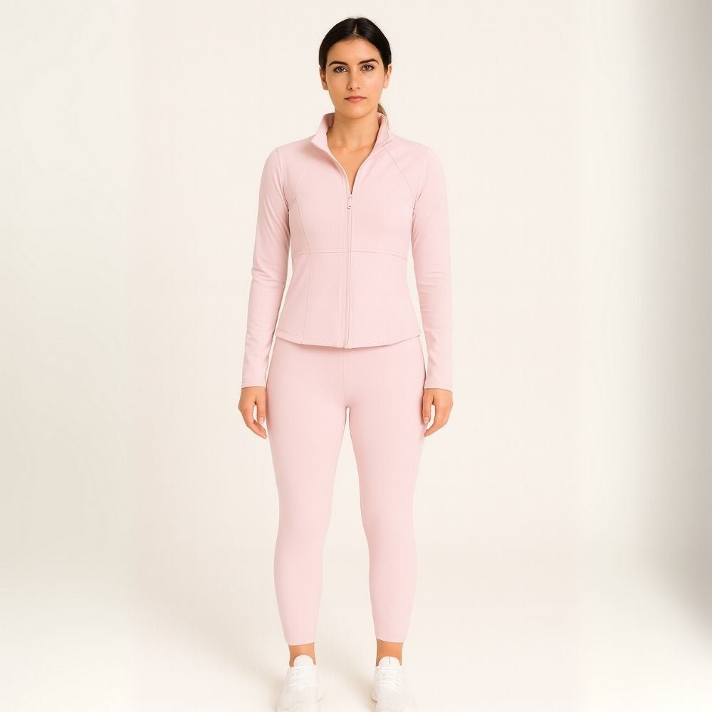 Woman wearing the Kouvr Sculpting Zip Jacket in Petal Pink against a white wall.