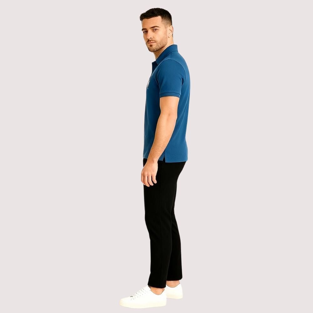Man wearing a blue kouvr polo shirt and black pants on a white background