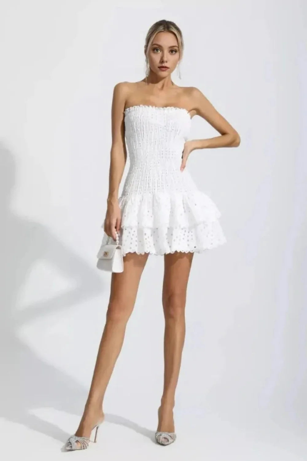 Model wearing the Kouvr Starla white strapless smocked mini dress with a tiered broderie anglaise ruffle skirt