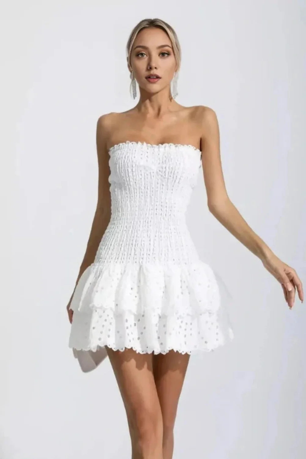 Model wearing the Kouvr Starla white strapless smocked mini dress with a tiered broderie anglaise ruffle skirt