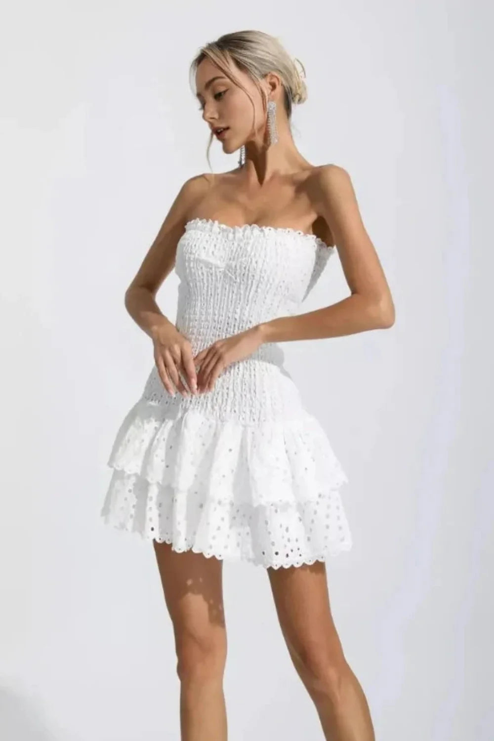 Model wearing the Kouvr Starla white strapless smocked mini dress with a tiered broderie anglaise ruffle skirt
